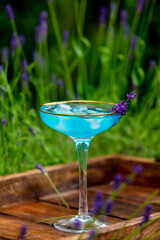 blue cocktail with ice and lavender on a tray in a garden