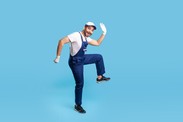 Full length funny happy handyman in blue uniform striding in big step, smiling crazy comical and...