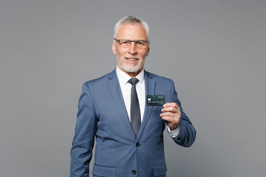 Successful elderly gray-haired mustache bearded business man in classic blue suit shirt tie isolated on grey wall background studio. Achievement career wealth business concept. Hold credit bank card.