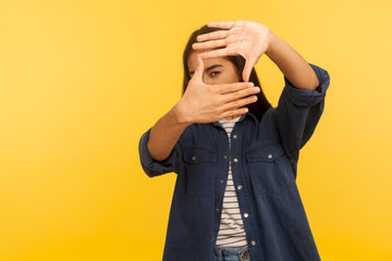 Portrait of girl in denim shirt looking through finger frame, imitating to take photo, focusing and...