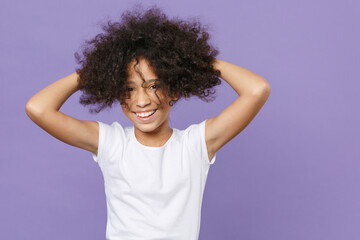 Cheerful little african american kid girl 12-13 years old in white t-shirt isolated on violet background children studio portrait. Childhood lifestyle concept. Mock up copy space. Put hands on head.