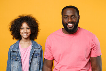 Smiling african american guy girl brother sister in denim pink clothes posing isolated on yellow wall background studio portrait. People emotions lifestyle concept. Mock up copy space. Looking camera.