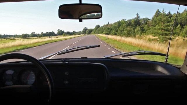 Interior view of an old retro unic AZLK Moskvich 2140 car driving fast at 100 on a new and slim asphalt highway in summer with clear blue sky, sunshine, fields and forest on roadsides