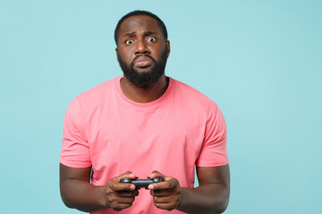 Displeased young african american man guy in casual pink t-shirt isolated on blue background studio portrait. People sincere emotions lifestyle concept. Mock up copy space. Play game with joystick.