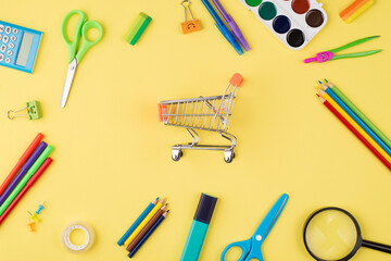 Back to school shopping concept. Top above overhead view photo of small cart and colorful stationery isolated on yellow background
