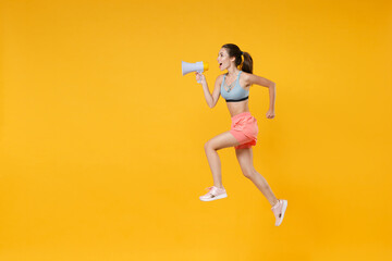 Full length portrait excited young fitness woman in sportswear working out isolated on yellow background. Workout sport motivation lifestyle concept. Mock up copy space. Jump, screaming in megaphone.