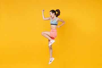 Fototapeta na wymiar Full length portrait of happy fitness girl in sportswear working out isolated on yellow background. Workout sport motivation lifestyle concept. Mock up copy space. Jumping clenching fists like winner.