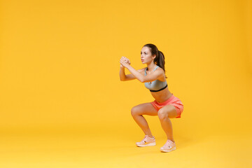 Fototapeta na wymiar Full length portrait of strong young fitness woman in sportswear working out isolated on yellow background. Workout sport motivation lifestyle concept. Mock up copy space. Doing exercise squatting.