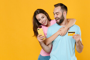 Excited young couple two friends guy girl in blue pink t-shirts isolated on yellow background...