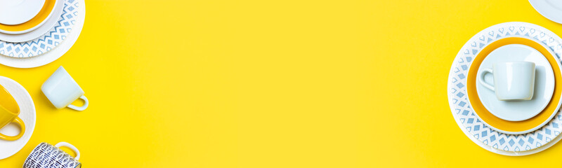 A lot of different ceramic dishes, empty coffee pairs, plates, cups on a bright yellow background. Wide banner or background with copy space.