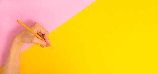 The left hand is holding a pencil and is about to write something on a bright pink-yellow background banner. International Left-handers Day on August 13.