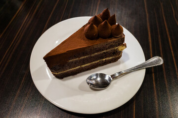 Piece of chocolate and cocoa cake on white plate and silver spoon