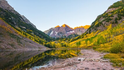 Maroon Bells lake sunlight on peak morning sunrise timelapse time lapse wide angle view with trees reflection in Aspen, Colorado with rocky mountains and autumn fall yellow foliage panoramic view