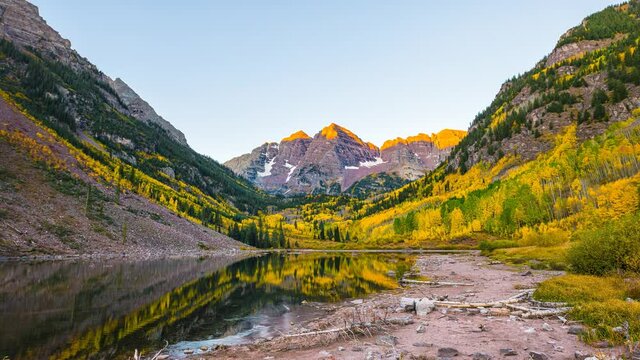 Maroon Bells lake sunlight on peak morning sunrise timelapse time lapse wide angle view with trees reflection in Aspen, Colorado with rocky mountains and autumn fall yellow foliage panoramic view