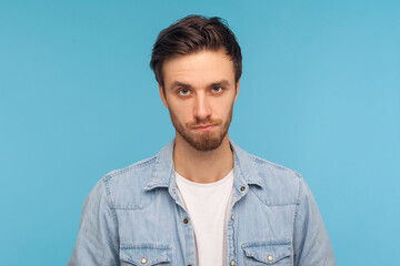 Portrait of unhappy man with bristle in worker denim shirt looking at camera with sad frustrated expression, feeling depressed, upset about troubles. indoor studio shot isolated on blue background