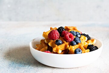 Tiny (Mini) waffles for breakfast with berries in a white bowl on a light background.