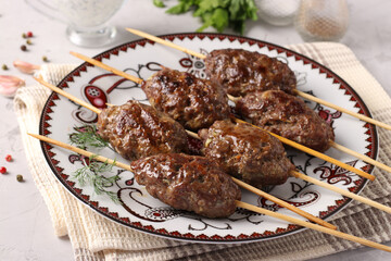 Kofta kebab on wooden skewers on a plate and sauce on the table, traditional dish of Arab cuisine, grilled minced meat shish kebab