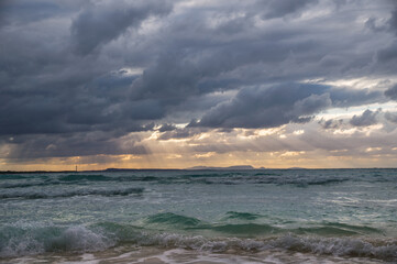 Stormy dark clouds above the sea with sandy beach and curling waves