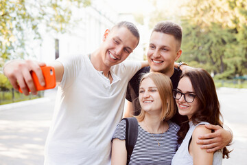 Group of young smiling friends in casual сlothes, taking selfie on a smartphone in student campus. Concept of friendship, education, youth and social communication.