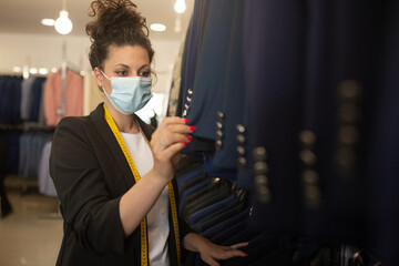 brunette clerk woman with curly hair and a virus mask, looking at blue suits 
