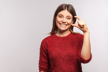 Portrait of cheerful brunette girl in shaggy sweater making little bit gesture, measuring small...