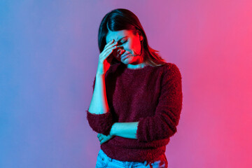 Neon light portrait of upset depressed young woman holding her head down, touching face and crying with dramatic grimace, feeling sorrow regret, desperate emotions. indoor studio shot isolated