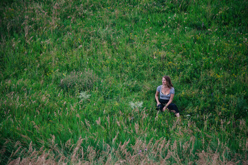 Beautiful girl in a black long skirt and striped T-shirt sitting on the slope of a green meadow