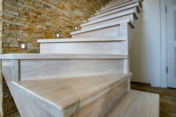 Stylish wooden contemporary staircase inside loft house interior. Modern hallway with decorative limestone brick walls and white oak stairs.