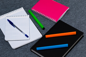 Notebooks, glider, pen and markers in different colors on a neutral gray fabric background. Fabric Max. School and business supplies. Office inventory. Subjects for the study. College.