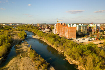 Fototapeta premium Aerial view of tall residential apartment buildings under construction and Bystrytsia river in Ivano-Frankivsk city, Ukraine.