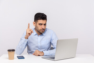 Be careful! Serious bossy businessman sitting office workplace with laptop on desk, showing finger up warn gesture and looking at camera alarming. indoor studio shot isolated on white background