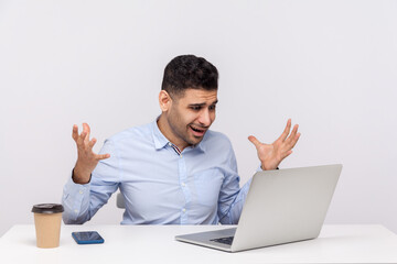 How could you? Angry annoyed businessman sitting office workplace, raising hands in indignant gesture, asking what why and looking at laptop screen, talking on video call. indoor studio shot isolated