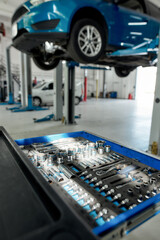 Little care for big mistakes. Close up shot of set of adjustable metallic tools for car repair in box. Vehicle repair kit with ratchet handle and sockets. Lifted car in the background