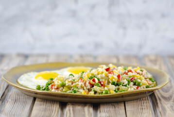 Rice with vegetables pepper, peas, corn and fried eggs on a plate. Place for text.