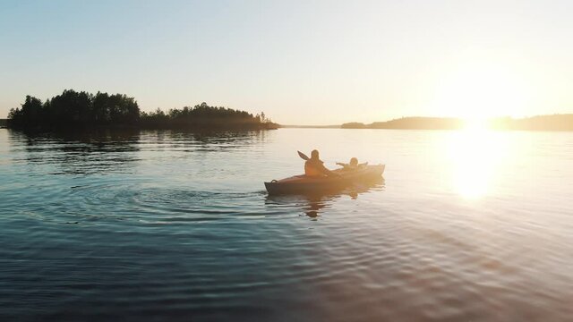 aerial drone flies around the kayak, young woman photographs a preschooler child in a boat against the background of a stunning sunset on the lake, outdoor activities