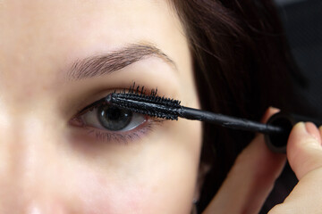 Naklejka premium beautiful girl paints eyes with mascara close-up. cosmetics, personal care