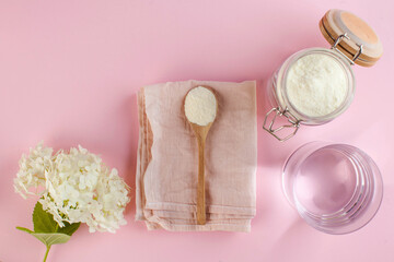 collagen powder in a wooden spoon on a pink background, a glass of water, flower. Skin care, rejuvenation. Copy space.