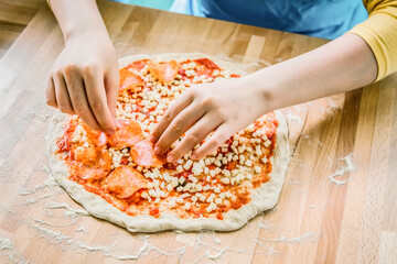 Italian cuisine. Fresh tasty pizza preparation. Female hands putting pepperoni on pizza.