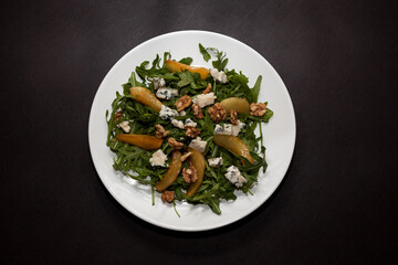 Arugula salad with warm caramelized pear, walnuts and blue cheese, dressed with lemon-honey sauce. Top view, dark background, copy space