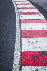 A white line on the right side of asphalt road with red and white painted curbs on the edge. Road turn traffic lines, race course road marking vertical background concept.