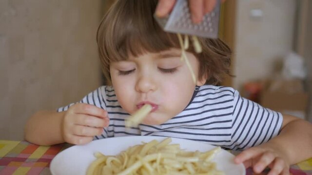 Cute Little Boy Eating Spaghetti With Cheese On Kitchen. Portrait Funny Healthy Preschool Kid Boy Eats Pasta Noodles. Hungry Child Eating With Hands And Smiling Healthy Food At Home.