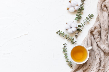 Cozy minimalism style composition with warm blanket, cup of herbal tea, cotton flowers and...