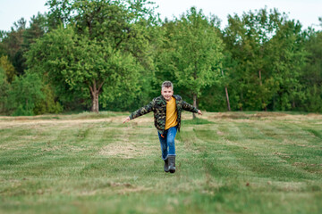 A boy runs across the field with his arms outstretched against a background of greenery. The concept of dreams, choice of profession, pilot, childhood. Copy space.