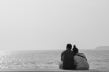 Back view of couple sitting on the floor and looking at the sea in Marine Drive, Mumbai. Picture in black and white.