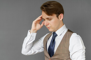 An emotional portrait of a businessman who touches his head with his hands. Gray background