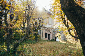 Obraz premium Sunshine portrait of happy bride and groom outdoor in nature location at sunset. Warm summertime. Happy couple with a beautiful bouquet of flowers. Wedding photo. Couple in love. Autumn wedding