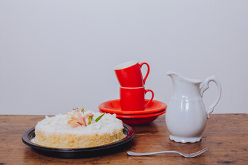 Brazilian coconut cake on a wooden table with dishes and red cups.