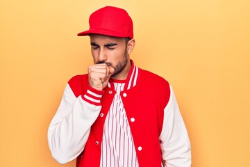 Handsome sporty man with beard wearing baseball jacket and cap over yellow background feeling unwell and coughing as symptom for cold or bronchitis. Health care concept.