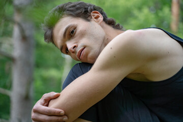 Side view of thoughtful man looking away while hugging knees in forest