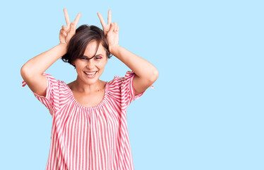 Beautiful young woman with short hair wearing casual summer clothes posing funny and crazy with fingers on head as bunny ears, smiling cheerful